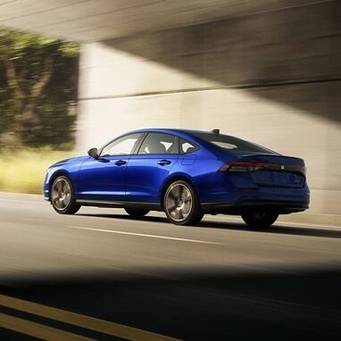 2026 Honda Accord in Still Night Pearl, rear 3/4 view, driving out from under the overpass.
